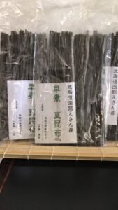 「早煮昆布」と書かれた100g入りの乾燥昆布のパッケージが、棚に縦にきれいに並べられている。パッケージには日本語で書かれたラベルが付いており、北海道恵山の品質の高さをアピールしている。.