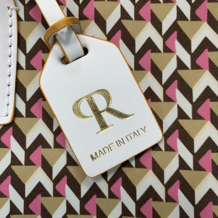 Un prim-plan al unei etichete de bagaje albe Roberta Pieri cu litera "R" în auriu și cuvintele "MADE IN ITALY" atașate la o mini geantă cu modele geometrice maro, bej și roz.