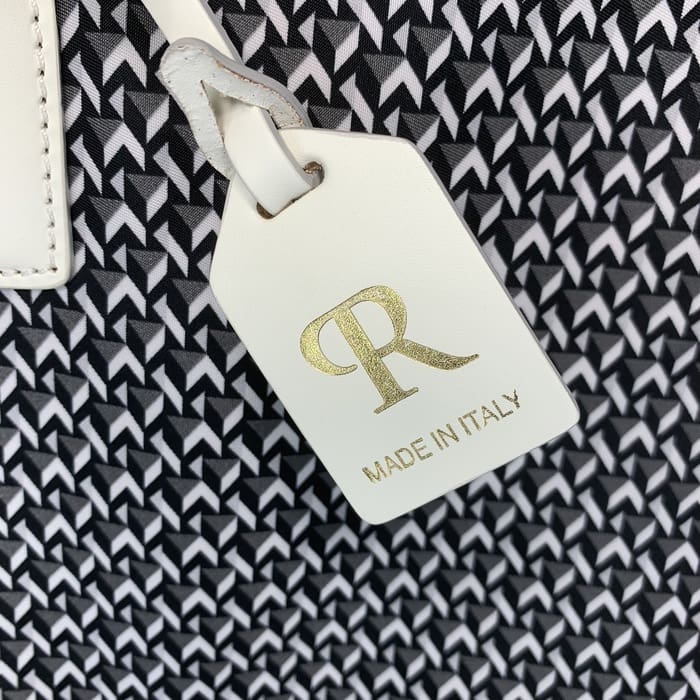 O etichetă ROBERTA PIERI din piele albă cu literele "R" în aur și cuvintele "MADE IN ITALY" atârnă de fundalul unei țesături geometrice alb-negru.
